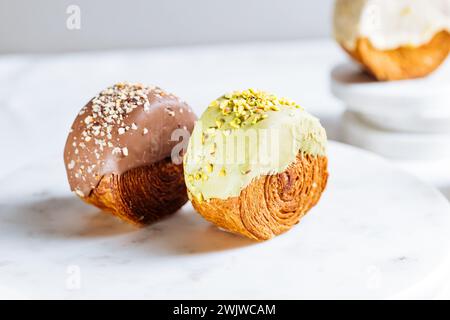 Fusion Croissant süßes Gebäck Cromboloni. New York Dessert. Runder Blätterteig mit Sahne gefüllt und mit weißer Milchschokolade oder Pistazien glasiert Stockfoto