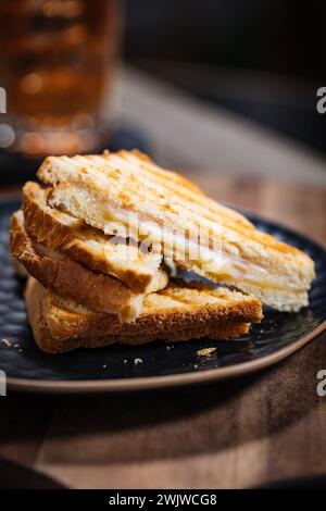 Geschnittenes Toast-Sandwich mit geschmolzenem Gouda-Käse und putenschinken auf hölzernem Hintergrund mit Kirschtomaten auf einem schwarzen Teller. Serviert mit Eistee. Stockfoto