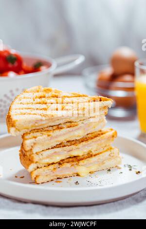 Geschnittenes Toast-Sandwich mit geschmolzenem Gouda-Käse putenschinken auf einem hellen Hintergrund mit Zutaten Tomaten-Orangensaft-Eiern im unscharfen Hintergrund Stockfoto