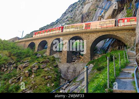 Roter Zug, der an der Teufelsbrücke in St. vorbeifährt Gotthard Pass auf den Schweizer Alpen in Andermatt, Schweiz Stockfoto