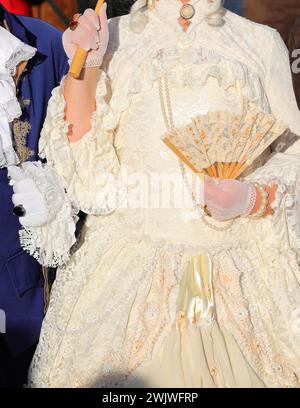Edelfrau mit luxuriösem, historischem Kleid aus Elfenbein und einem Fan in Handschuhen während der Party in Venedig Italien Stockfoto