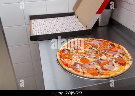 Frische heiße Pizza mit Wurst, Schinken, Pilzen, Paprika, Tomaten und Mozzarella auf dem Tisch in der Pizzeria. Italienische Küche, hausgemachte Bäckerei Stockfoto