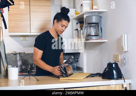 Junger Latein-Mann in der Küche zu Hause, der frisch gebackenen Kuchen aus der Form herausnimmt und ihn auf das Schneidebrett auf den Tisch legt. Stockfoto