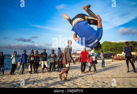 Ein junger Mann spielt Akrobatik am späten Nachmittag am Strand in Stone Town, Sansibar, Tansania. Stockfoto