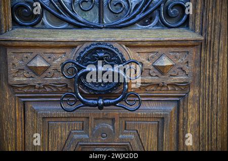 Türgriff aus Gusseisen im Retro-Stil an einer antiken, handgeschnitzten Eichenholztür in Turckheim, Elsass Frankreich. Stockfoto