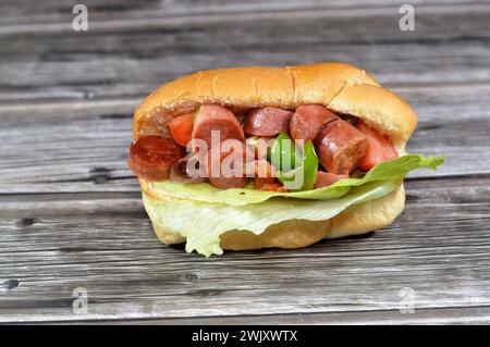 Teilweise geschnittenes Hotdog-Brötchen mit Scheiben von gegrilltem Rinderwurst, genannt wiener (Wiener Wurst) und frankfurter Frank, mit Tomatenscheiben, o Stockfoto