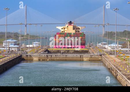 Colon, Panama - 23. Januar 2024: Agua Clara schließt den Panamakanal ab. Im Hintergrund befindet sich ein Containerschiff und die Atlantikbrücke Stockfoto