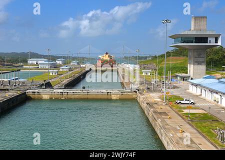 Colon, Panama - 23. Januar 2024: Schleusen und Kontrollturm von Agua Clara am Panamakanal. Im Hintergrund befindet sich ein Containerschiff und die Atlantikbrücke Stockfoto