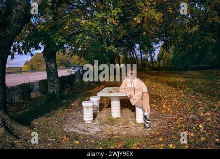 Eine reife, hübsche Frau sitzt neben einem Tisch in einem Parkplatz in der Nähe einer Landstraße in Frankreich. Herbstlandschaft Stockfoto