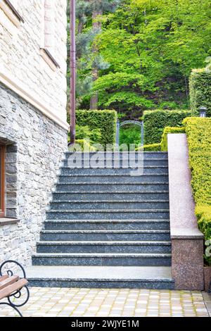 Die Stufen der Steintreppe, die zum Park führt, sind am Hang entlang der Hauswand und getrimmten Buchsbaumbüschen angelegt. Stockfoto