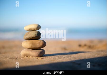 Stillleben mit gestapelten Kieselsteinen, Steinen am Sandstrand vor dem Hintergrund des Atlantischen Ozeans mit Wellen, die am Strand brechen. Das Konzept von h Stockfoto