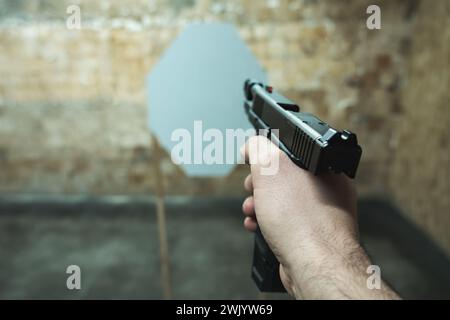 Eine Pistole in der Hand eines Mannes zielt auf ein Papierziel auf einen Schießstand. Hochwertige Fotos Stockfoto