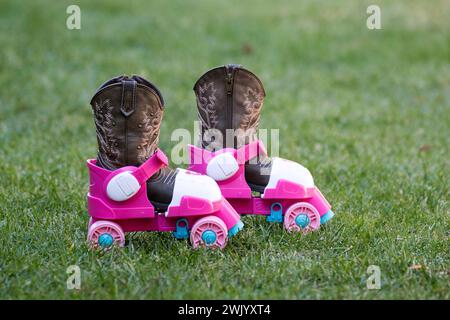 Die rosa Plastik-Rollschuhe eines kleinen Mädchens waren auf dem grünen Rasen, und ihre Cowboystiefel waren noch in den Rollschuhen. Stockfoto