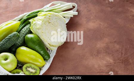Frisches grünes Obst und Gemüse in Mesh Bag auf Ton Hintergrund, Kopierraum Stockfoto