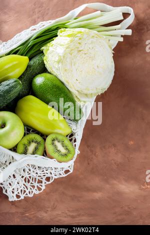 Frisches grünes Obst und Gemüse in Mesh Bag auf Ton Hintergrund, Kopierraum Stockfoto