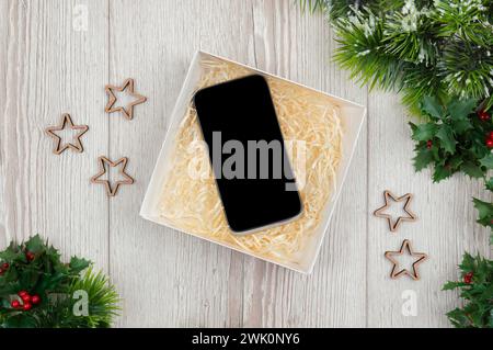 Modisches Smartphone-Geschenk. Weihnachtsgeschenk und Mockup des Smartphones auf hölzernem Hintergrund. Flache Lage, Ansicht von oben. Black Friday Sale Shopping-Konzept Stockfoto