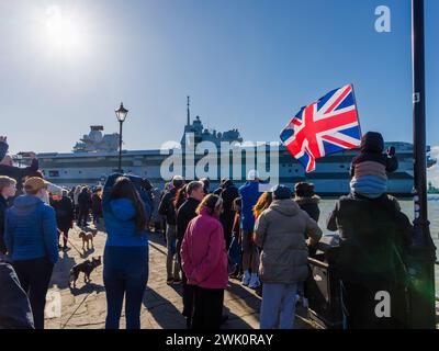 Ein Junge, der auf den Schultern seines Vaters sitzt, winkt einen Union Jack, während der Flugzeugträger der Queen Elizabeth-Klasse „HMS Prince of Wales“ von Portsmouth Harbour abfährt Stockfoto