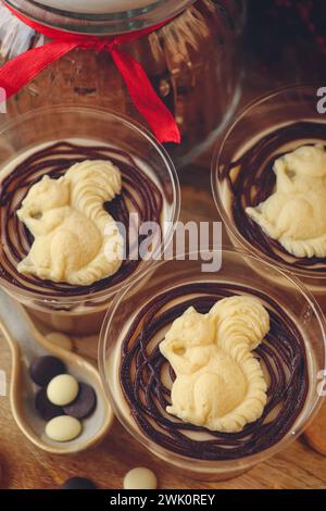 Italienisches Dessert Panna Cotta mit Schokoladenbelag. Panna Cotta verziert mit weißem Schokoladenhörnchen auf hölzernem Hintergrund. Stockfoto