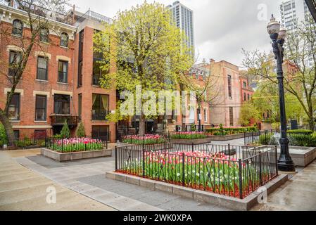 Kleiner Platz mit Blumenbeeten und einem Brunnen, umgeben von Backsteingebäuden in der Altstadt von Chicago an einem bewölkten Frühlingstag Stockfoto