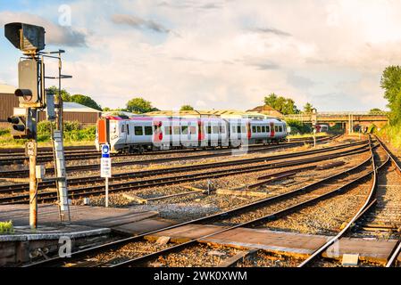 Diesel-Personenzug, der im Sommer bei Sonnenuntergang einen Bahnhof verlässt. Zwei weitere Züge sind in der Entfernung sichtbar. Stockfoto