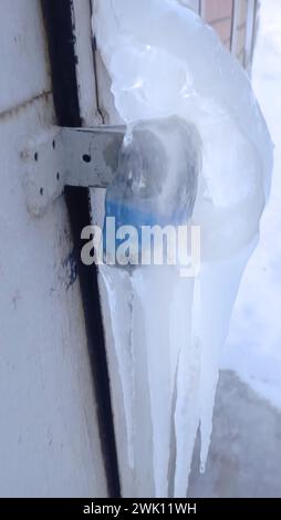 Ein Vorhängeschloss an einer Metalltür vor einem Gebäude, bedeckt mit Eis. Stockfoto