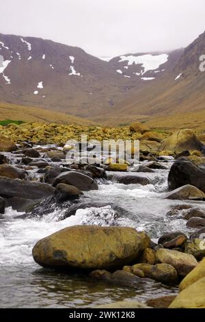 Der Fluss stürzt über Felsen im Vordergrund mit einsamen Berghängen im Hintergrund in der Tablelands-Region des Gros Morne-Nationalparks Stockfoto