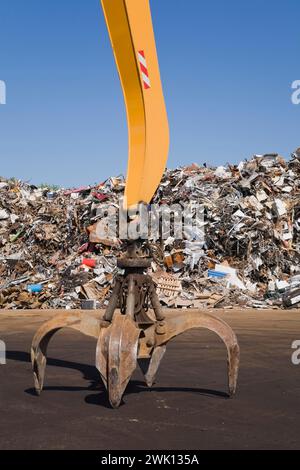 Greiferarm mit Klauenklammer vor dem Stapel von Altmetall-Haushalts- und Industrieartikeln auf dem Altmetallrecyclingplatz. Stockfoto