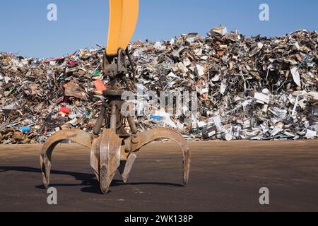 Greiferarm mit Klauenklammer vor dem Stapel von Altmetall-Haushalts- und Industrieartikeln auf dem Altmetallrecyclingplatz. Stockfoto