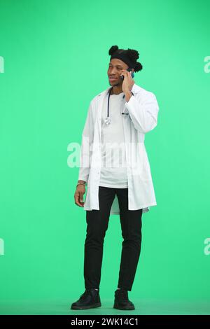 Der Doktor, in voller Höhe, auf grünem Hintergrund, spricht am Telefon Stockfoto