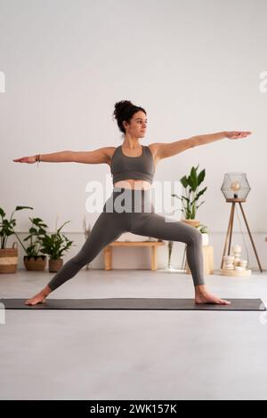 Kaukasische Frau in grauem Sportoutfit, die zu Hause Yoga-Übungen macht und Warrior-Pose macht. Stockfoto