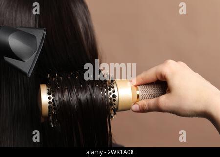 Friseur föhnt das Haar des Kunden auf hellbraunem Hintergrund, Großaufnahme Stockfoto