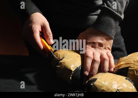 Schmuggel und Drogenhandel. Mann, der ein Paket mit Betäubungsmitteln öffnet, mit einem Koffer in der Dunkelheit, Nahaufnahme Stockfoto