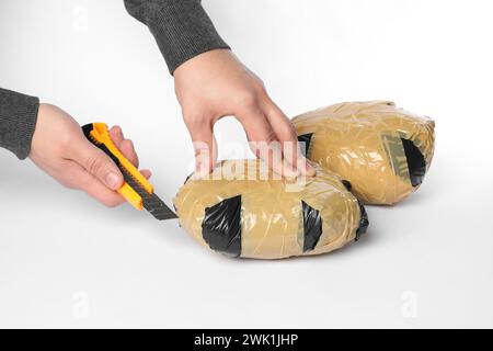 Schmuggel und Drogenhandel. Mann, der ein Paket mit Betäubungsmitteln mit einem Koffer auf weißem Hintergrund öffnet, Großaufnahme Stockfoto