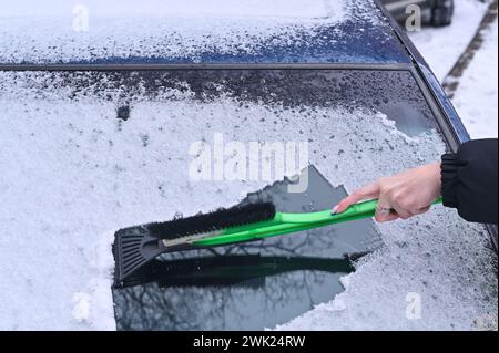 Die Hand einer Frau mit einem Schaber entfernt Eis aus dem Autofenster Stockfoto