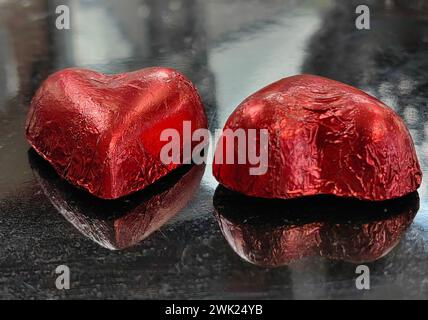 Zuckerdichotomie. Geschlechtsspezifische Reflexionen. Zwei herzförmige Schokoladenbonbons auf schwarzem Tisch, die Mann und Frau symbolisieren. Alles Gute zum Valentinstag. Stockfoto