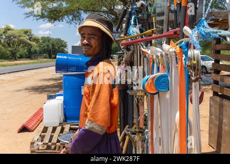 Straßenverkäufer afrikanischer Mann mit Zöpfen, der Hardware verkauft. Riemen und Trommeln am Straßenrand Stockfoto