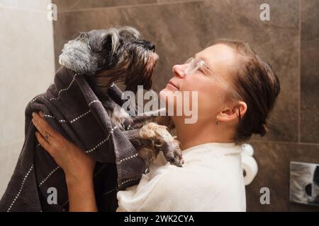 Frau im Badezimmer mit ihrem kleinen Schnauzer Hund, Stockfoto