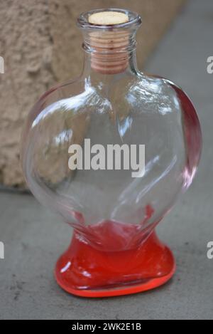 Ein wunderschönes Glasgefäß in Herzform mit einem leichten Holzstopfen und einer roten adstringenten Flüssigkeit steht auf der Straße. Stockfoto