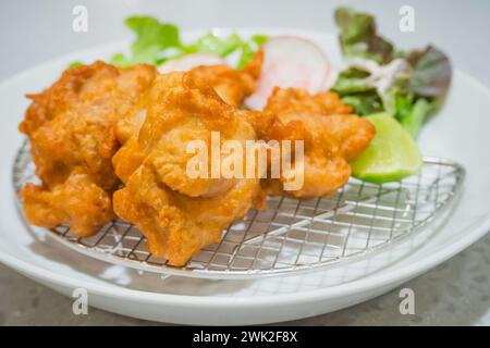 Gebratenes Hühnchen auf japanischer Art mit Gemüse und Zitrone auf weißem Teller Stockfoto