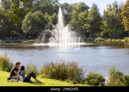 Das junge Paar sitzt auf dem Gras in der Nähe eines Teichs im Vondelpark in Amsterdam. Stockfoto