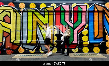 Ein junges Paar, das sich vor einem Graffiti-Wandgemälde in Shoreditch, East London streitet Stockfoto