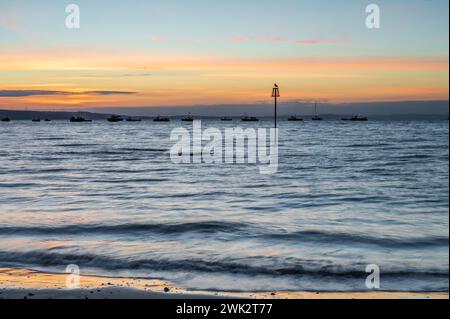 Sommersonnenaufgang über Tenby South Beach, Wales, Großbritannien. Die Sonne geht über einem ruhigen Meer auf und färbt den Himmel orange und rot. Es ist ein einzelner Posten sichtbar Stockfoto