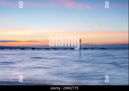 Sommersonnenaufgang über Tenby South Beach, Wales, Großbritannien. Die Sonne geht über einem ruhigen Meer auf und färbt den Himmel orange und rot. Es ist ein einzelner Posten sichtbar Stockfoto