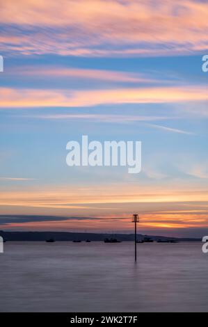 Sommersonnenaufgang über Tenby South Beach, Wales, Großbritannien. Die Sonne geht über einem ruhigen Meer auf und färbt den Himmel orange und rot. Es ist ein einzelner Posten sichtbar Stockfoto