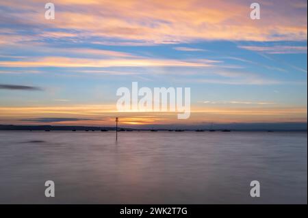 Sommersonnenaufgang über Tenby South Beach, Wales, Großbritannien. Die Sonne geht über einem ruhigen Meer auf und färbt den Himmel orange und rot. Es ist ein einzelner Posten sichtbar Stockfoto