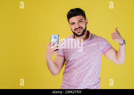 Brünette, gutaussehender Mann mit Bart, der drinnen posiert, lächelt, das Smartphone hält, fotografiert. Stockfoto