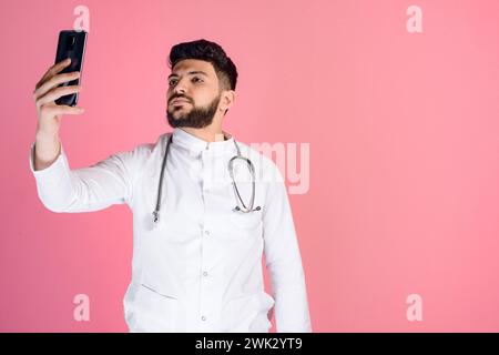 Hübscher junger Arzt, Praktikant in Uniform stehend, Hand heben, Selfie machen. Stockfoto