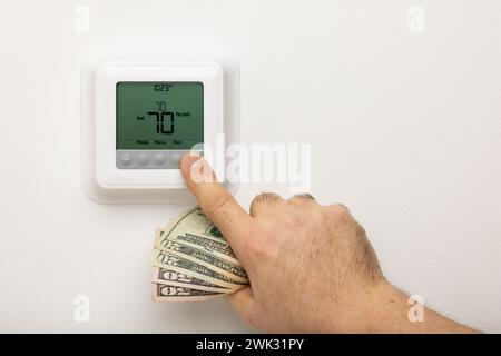 Eine Hand, die Geld hält, um einen Thermostat einzustellen. Stockfoto