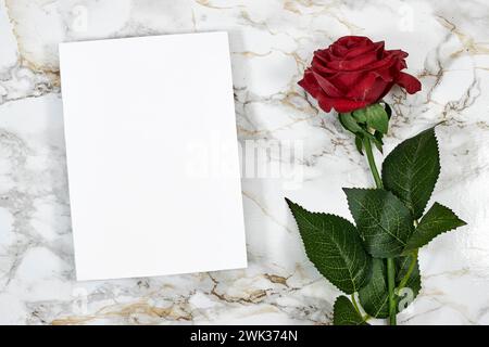 Hochzeitseinladungskarte Mockup und roter Umschlag mit roter Rose auf Marmorhintergrund. Leeres Kartenmodell Stockfoto