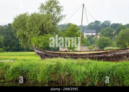 Ein altes, verwittertes Holzboot liegt an Land inmitten von üppigem Grün unter einem bewölkten Himmel in einer ruhigen ländlichen Umgebung Stockfoto